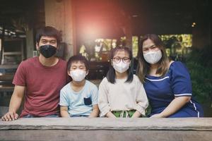 Família asiática usando máscara protetora sentada em casa tailandesa foto