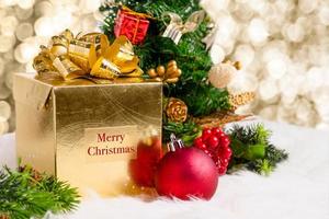 caixa de presente ouro brilhante com palavra de feliz natal e decoração vermelha foto