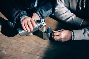 casal de idosos com mãos servindo café da garrafa térmica foto