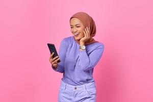 retrato de uma jovem asiática sorridente segurando um telefone celular no fundo rosa foto