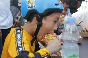 Indonésia - Medan, 17 agosto 2023 a ásia Garoto vestindo uma capacete é comendo uma quente cachorro foto