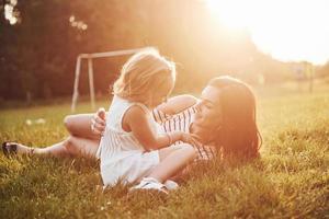 feliz mãe e filha se abraçando em um parque ao sol em um fundo de verão brilhante de ervas. foto