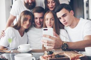 um grupo de pessoas tira uma foto de selfie em um café. os melhores amigos reunidos em uma mesa de jantar comendo pizza e cantando vários drinks