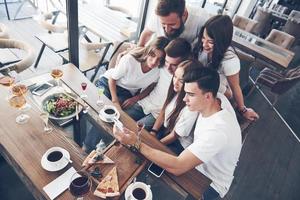 um grupo de pessoas tira uma foto de selfie em um café. os melhores amigos reunidos em uma mesa de jantar comendo pizza e cantando vários drinks