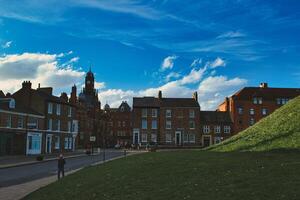 pitoresco europeu Cidade com histórico edifícios debaixo uma dramático azul céu com fofo nuvens, apresentando uma exuberante verde Colina e pedestres em uma calçada dentro Iorque, norte yorkshire, Inglaterra. foto