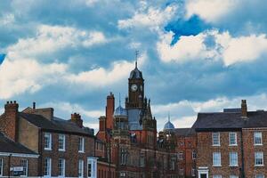 dramático nuvens tear sobre uma histórico Cidade Centro, apresentando uma proeminente relógio torre e clássico tijolo edifícios, capturando uma quintessencial britânico paisagem urbana dentro Iorque, norte yorkshire, Inglaterra. foto