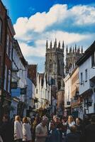 movimentado rua cena com pedestres dentro uma histórico cidade Centro, apresentando velho edifícios e uma proeminente gótico catedral debaixo uma nublado céu dentro Iorque, norte yorkshire, Inglaterra. foto