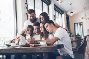 um grupo de pessoas tira uma foto de selfie em um café. os melhores amigos reunidos em uma mesa de jantar comendo pizza e cantando vários drinks