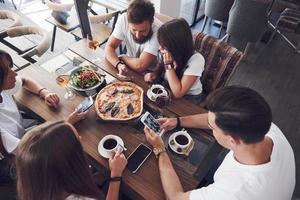 pizza saborosa na mesa, com um grupo de jovens sorridentes descansando no bar foto