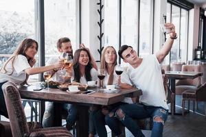 um grupo de pessoas tira uma foto de selfie em um café. os melhores amigos reunidos em uma mesa de jantar comendo pizza e cantando vários drinks