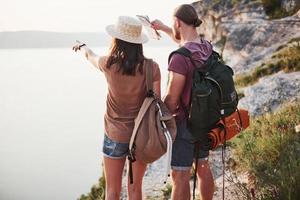 dois turistas homem e mulher com mochilas estão no topo do rochedo e aproveitando o nascer do sol. viajar montanhas e costa, liberdade e conceito de estilo de vida ativo foto