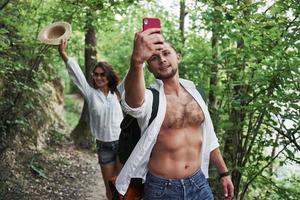 dois caminhantes com mochilas nas costas na natureza. jovem casal homem e mulher fazem selfie passeio em um dia de verão foto