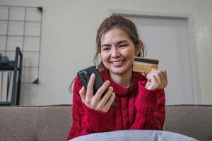 mulher segurando crédito cartão e usando Smartphone às lar, conectados compras, conectados bancário, pagamento, gastos dinheiro, comércio eletrônico às loja, crédito cartão conceito foto