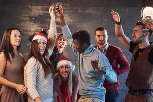 festa com amigos. eles amam o natal. grupo de jovens alegres carregando estrelinhas e taças de champanhe, dançando na festa de ano novo e parecendo feliz. conceitos sobre estilo de vida de união foto