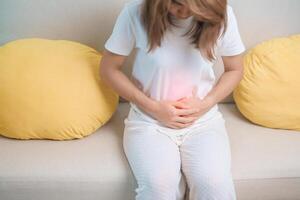 mulher tendo abdômen dor vencimento para estômago dor, digestão com constipação ou diarréia a partir de Comida envenenamento, fêmea problema e endometriose, histerectomia, dor de estômago e menstrual em sofá às casa foto