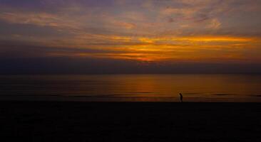 silhuetas uma sereno pôr do sol sobre a praia, a céu do laranja e fundição foto