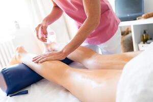 colheita massagista fricção pele do fêmea cliente perna com oleoso spray dentro clínica foto