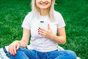 mulher com fones de ouvido e smartphone na grama verde foto