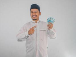 adulto muçulmano ásia homem sorridente e mostrando confiante quando apontando para papel dinheiro este ele aguarde foto