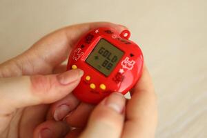 Kyiv, Ucrânia - marcha 9, 2024 retro animal chaveiro jogos tamagotchi dentro vermelho plástico caso dentro fêmea mãos foto