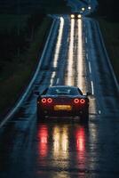 uma Esportes carro dirigindo baixa uma molhado estrada às noite foto