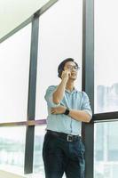empresário ao lado de uma grande janela dentro de um edifício moderno, falando no celular. foto