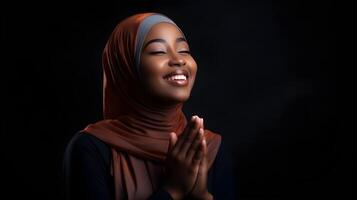 africano mulher vestindo cachecol é Rezar e sorridente em Preto fundo foto