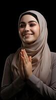 árabe mulher vestindo cachecol é Rezar e sorridente em Preto fundo foto