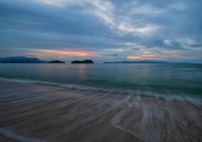 a Sol configuração sobre a oceano com pedras dentro a primeiro plano foto