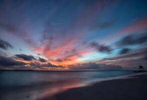 a Sol configuração sobre a oceano com pedras dentro a primeiro plano foto