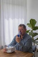 idosos homem sentado em uma mesa e usando uma nebulizador névoa às casa foto