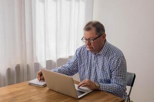 Senior homem trabalhando em computador portátil dentro a casa foto