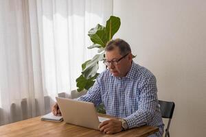 Senior homem trabalhando em computador portátil dentro a casa foto