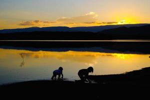 silhuetas de crianças felizes brincando no lago na hora do pôr do sol, reservatório amphoe wang saphung loei tailândia foto