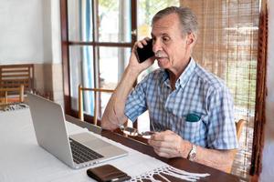 um homem idoso trabalha em um escritório com laptop em casa.