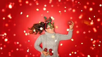 Natal ano novo. jovem vestida com uma camisola quente com adereços bola vermelha com enfeites de Natal em férias em fundo vermelho brilho. conceito, feliz Natal. foto