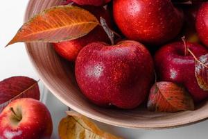 lindas maçãs vermelhas frescas com folhas de outono em um vaso de madeira foto