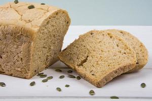 Pão rústico de fermento de trigo com sementes de abóbora no fundo branco da placa de madeira foto