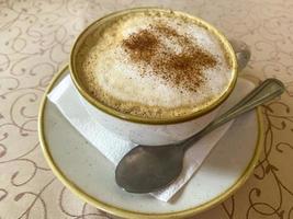 quente delicioso cappuccino com espuma e canela em copo vintage na mesa foto