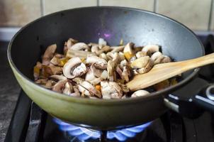 champignon com cebola são fritos na frigideira, fogo foto