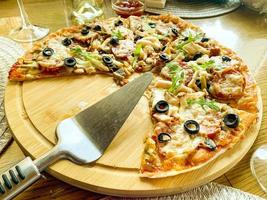 Fatias de pizza caseira com salame e azeitonas no prato de madeira foto