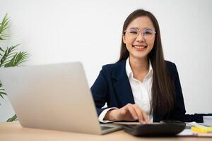 retrato do sorridente lindo o negócio ásia mulher às moderno escritório escrivaninha usando computador portátil para trabalhos e escrever notas, o negócio pessoas empregado freelance conectados marketing comércio eletrônico telemarketing conceito. foto