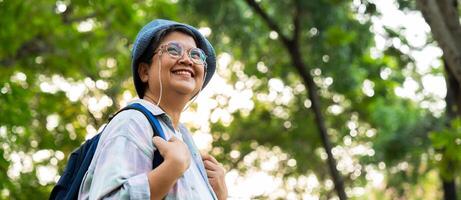 retrato do ásia maduro mulher dentro uma chapéu com mochila atrás dela voltar, a Ásia ativo Senior mulher desfrutando natureza dentro outono parque. em pé em uma trilha dentro uma floresta ao ar livre. desfrutando ativo viagem viagem foto