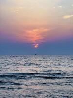 uma tranquilo oceano cena Como a Sol mergulhos abaixo a horizonte, pintura a céu com tons do Rosa e laranja foto
