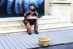 Baku, Azerbaijão - dezembro 02, 2023 . uma jovem cara com tranças e uma barba tocam uma percussão musical instrumento aguentar dentro a cidade em a rua. foto
