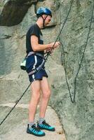 jovem homem dentro equipamento em pé dentro frente do pedra Rocha ao ar livre e obtendo pronto para escalar. Treinamento área para ao ar livre Atividades. extremo esporte. foto