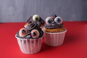 três bolos de copo com olhos em uma vermelho fundo. engraçado bolos para crianças dia das Bruxas festa com espaço para cópia de espaço texto foto