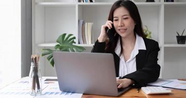 Mulher asiática de negócios usando smartphone para fazer finanças matemáticas na mesa de madeira no escritório, impostos, contabilidade, conceito financeiro foto