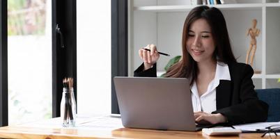 mulher asiática de negócios usando laptop para fazer finanças matemáticas na mesa de madeira no escritório, impostos, contabilidade, conceito financeiro foto