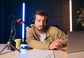 sorridente e gesticulando rádio hospedeiro com fones de ouvido lendo notícia a partir de papel para dentro estúdio microfone às rádio estação com néon luzes foto